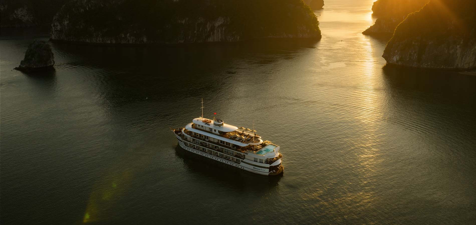 A festive luxury cruise sailing through Ha Long Bay at sunset